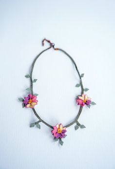 a necklace with pink flowers and green leaves is shown on a white surface, while the bead cord has been stitched together