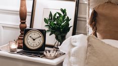 a clock sitting on top of a white table next to a vase with flowers in it