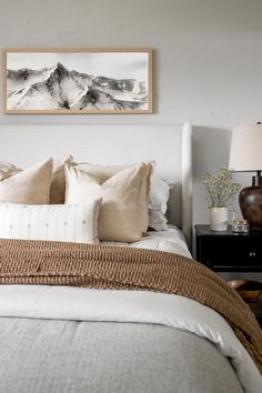 a bed with white linens and pillows in front of a painting on the wall