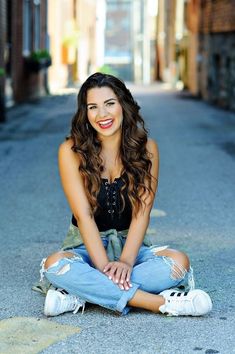 a young woman sitting on the ground with her legs crossed and looking at the camera