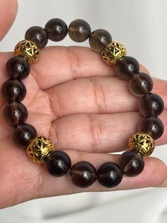 Crafted with intricate gold-toned beads and a clear stretchy string, the "Baroque" Smoky Quartz Bracelet is both elegant and versatile. Adorn your wrist with this stunning accessory that features exceptionally clear Smoky Quartz, known for its grounding, protective, and stress-relieving properties. Elevate any outfit with this timeless piece.