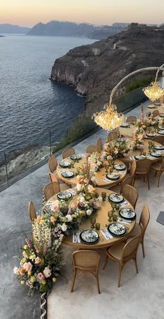 an outdoor dining table set up with flowers and plates on it, overlooking the ocean