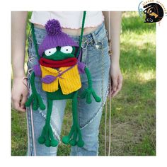 a crocheted frog purse with a purple hat and scarf hanging from it's back