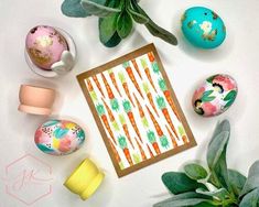 an easter card surrounded by painted eggs and greenery on a white surface with pastel colors