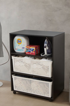 an ironing board next to two baskets with laundry products on them and a lamp in the background