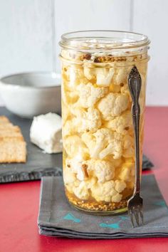 a glass jar filled with cauliflower sitting on top of a table next to crackers