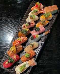 there are many sushi rolls on the wooden tray with different types of toppings