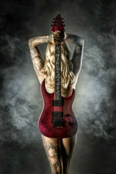 a woman with tattoos holding a guitar in front of her face and back to the camera