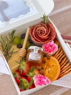 an open box filled with fruit, cheese and crackers next to a pink flower