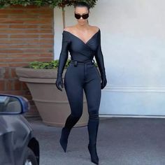 a woman in black is walking down the street wearing sunglasses and a bodysuit with long sleeves