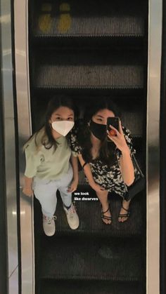 two women wearing face masks while riding an escalator