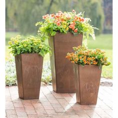 three planters with flowers in them sitting on a brick patio