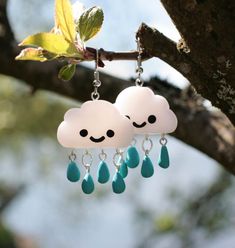 two clouds are hanging from a tree branch with blue tear drops dangling from the dangles