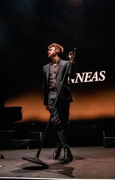 a man standing on stage with a microphone in his hand and wearing a black suit