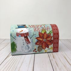 a christmas themed box with a snowman and poinsetti on the front, sitting on a wooden surface