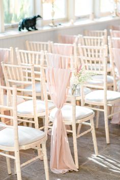 rows of white chairs with pink sashes and flowers in vases on the back