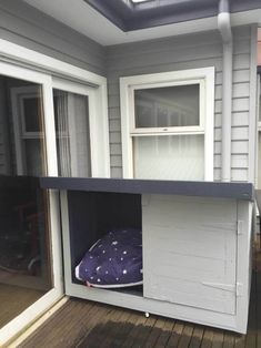 a dog house built into the side of a house with a purple pillow in it