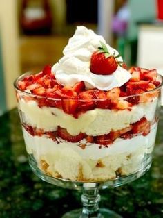 a trifle with strawberries and whipped cream in a glass dish on a table