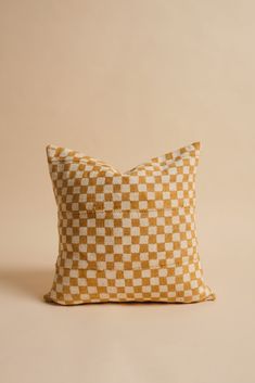 a yellow and white checkered pillow sitting on top of a beige surface with a tan background