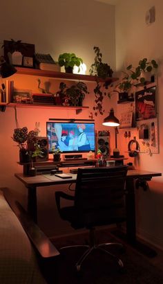 a desk with a computer on it and plants in the corner, all lit up