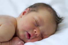 a close up of a baby sleeping on a white blanket with its eyes closed and mouth wide open