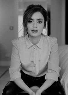 a woman sitting on top of a bed wearing black leather pants and a pink shirt