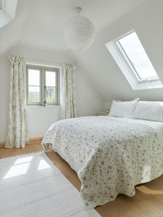 a white bed sitting under a window in a bedroom next to a rug on top of a hard wood floor