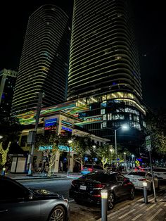 cars are parked on the street in front of high rise buildings at night with bright lights