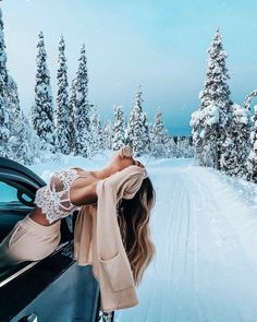 a woman leaning out the window of a car on a snowy road with trees in the background