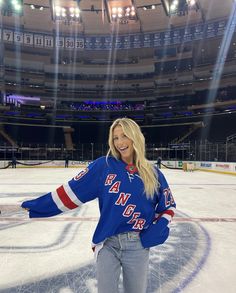 a woman standing on top of an ice rink wearing a blue hockey jersey with red and white stripes