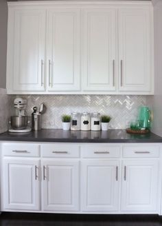 a kitchen with white cabinets and black counter tops in front of a gray tiled backsplash