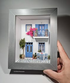 a hand holding up a miniature model of a house with blue shutters and balconies