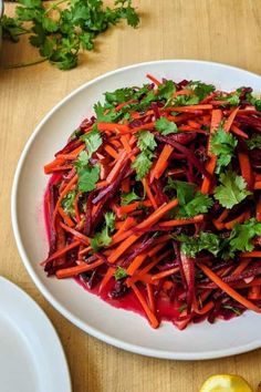 a white plate topped with carrots and cilantro next to lemon wedges