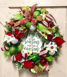 a christmas wreath with green and red decorations on the front door that says jesus is the reason for the season