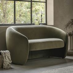 a green couch sitting in front of a window next to a table with a vase on it