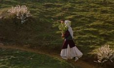 a woman walking down a dirt path with flowers in her hand