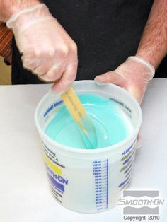 a man is mixing blue liquid in a bucket with a yellow spoon and plastic gloves