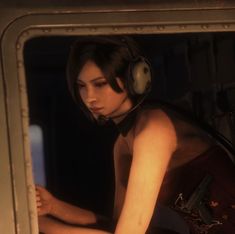 a woman wearing headphones sitting in front of a window with her hand on the keyboard