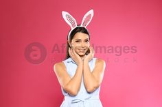 a woman wearing bunny ears talking on a cell phone while standing against a pink background