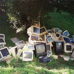 a pile of old televisions sitting on top of a green grass covered field next to a tree