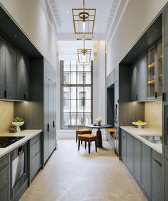 a long kitchen with gray cabinets and white counter tops, along with a dining room table