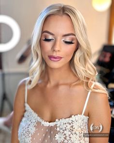 a woman with long blonde hair wearing a white dress and makeup looks at the camera