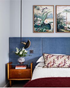 a bed with two paintings above it and a night stand next to the headboard