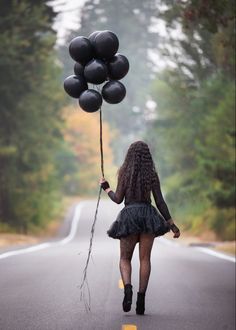 a woman walking down the road holding black balloons