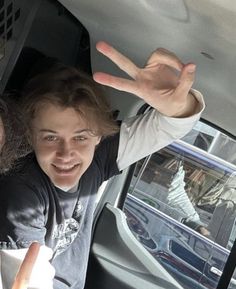 two people sitting in the back seat of a car with their hands up and one person pointing