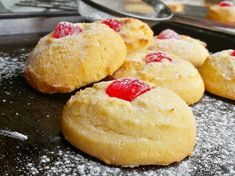 several cookies with cherries on them sitting on a baking sheet covered in powdered sugar