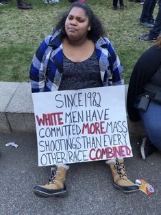 a woman sitting on the ground holding a sign