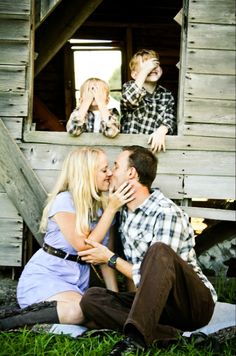 a man and woman sitting on the ground with two children looking at them through a window