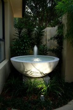 a white sink sitting in the middle of a garden next to a building and trees