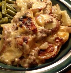 a close up of a plate of food with meat and cheese on it next to green beans